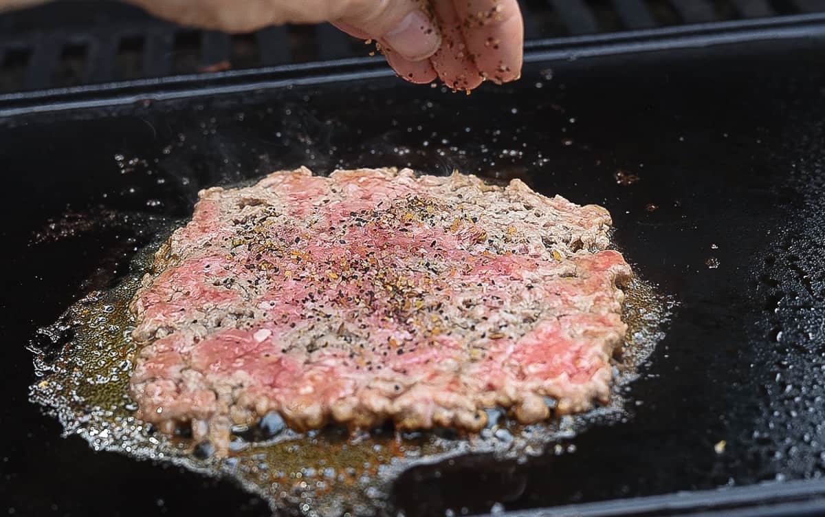 A smashed burger patty being seasoned.